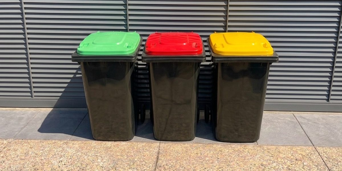 Three cleaned wheelie bins standing upright side by side with their lids closed