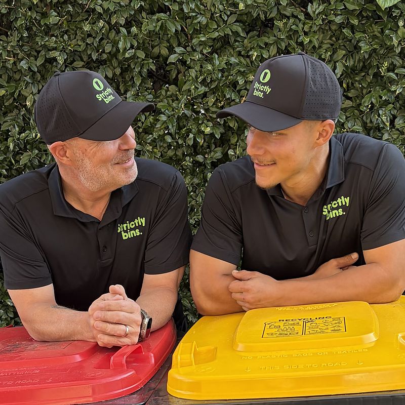 Simon and Michael, the father-and-son team behind Strictly Bins, in branded uniforms beside two wheelie bins